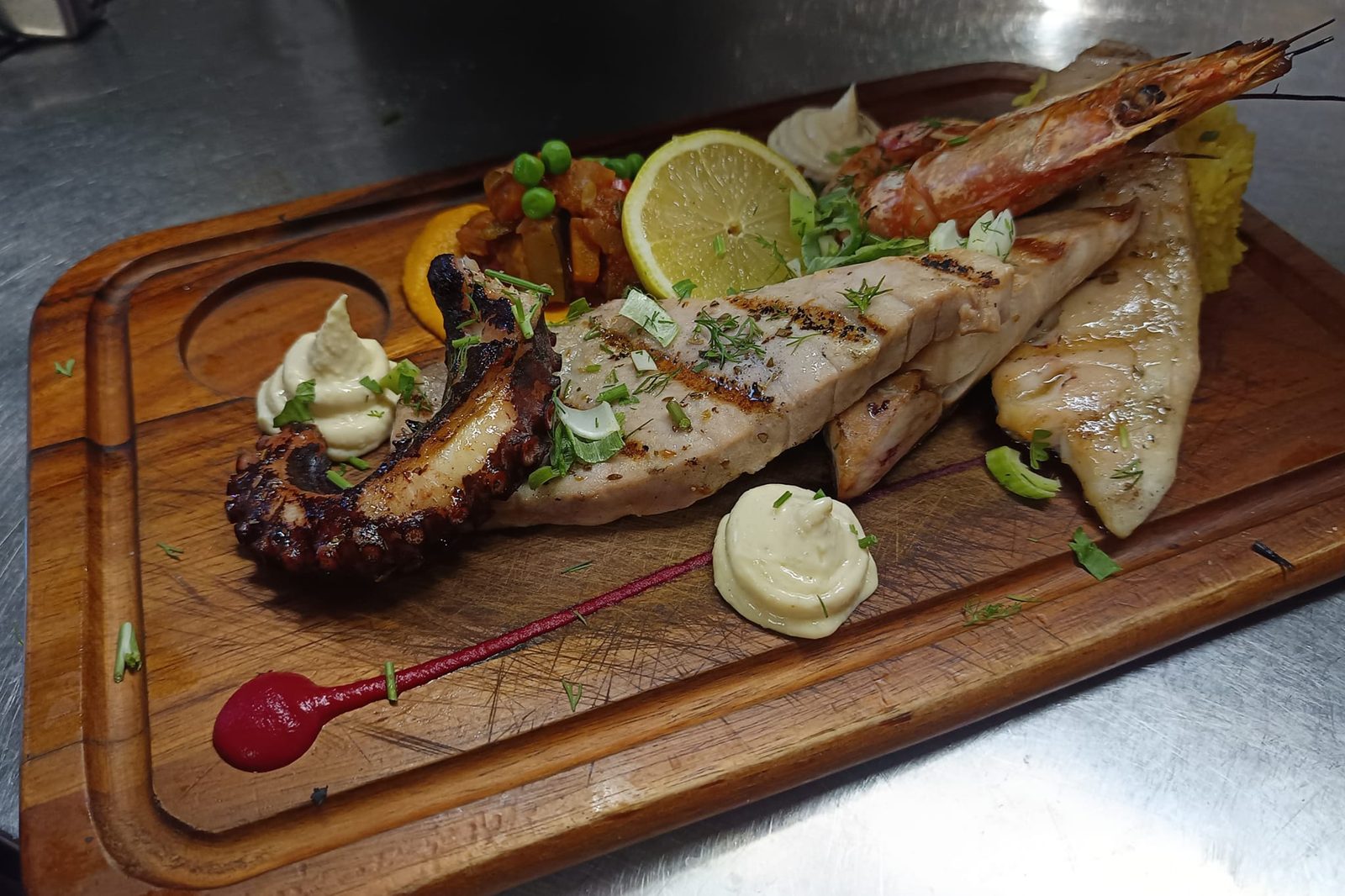 Une planche de grillades de poisson et de gambas, avec du citron et des sauces