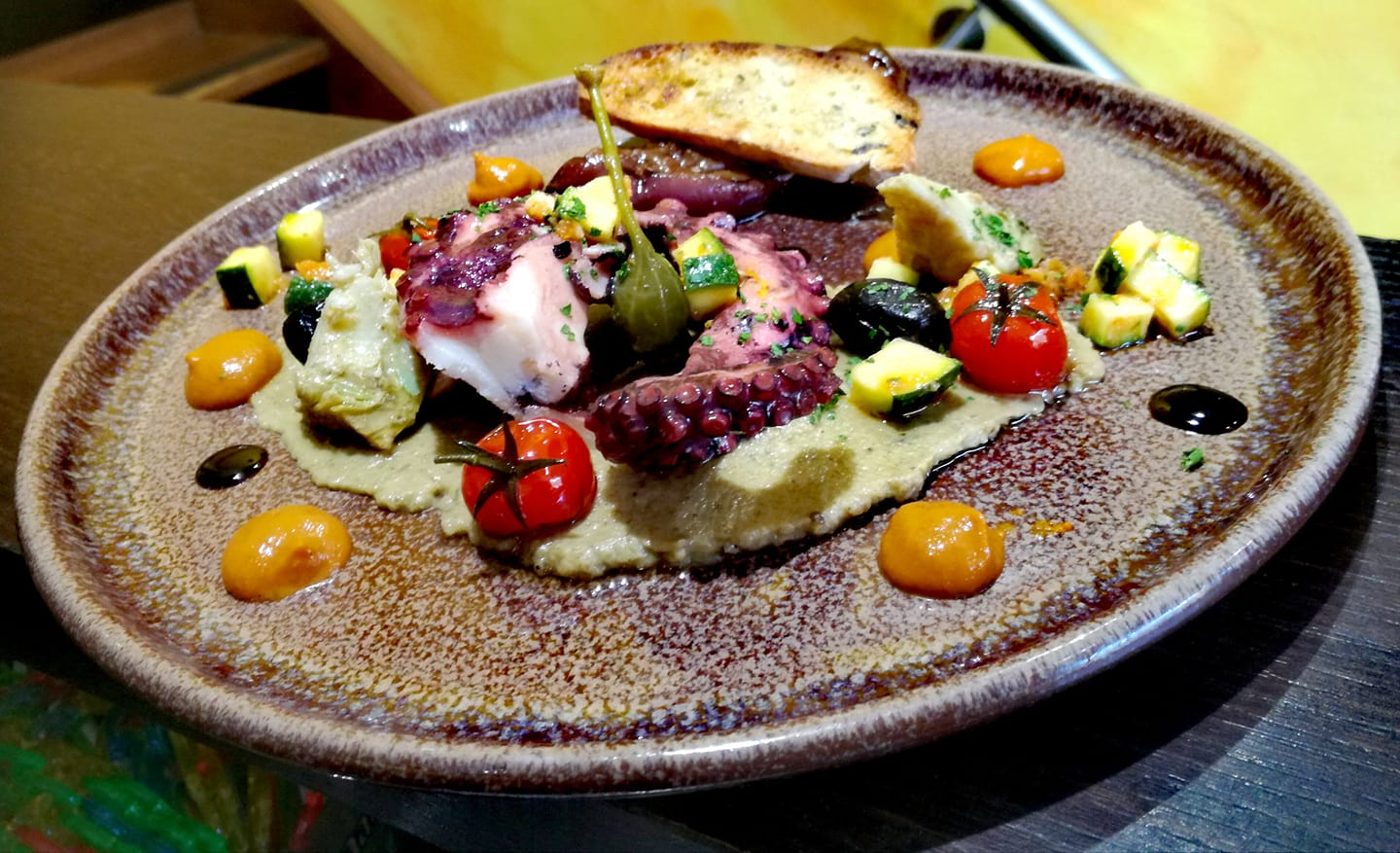 Du poulpe grillé sur une purée, avec des légumes colorés, dans une assiette ronde
